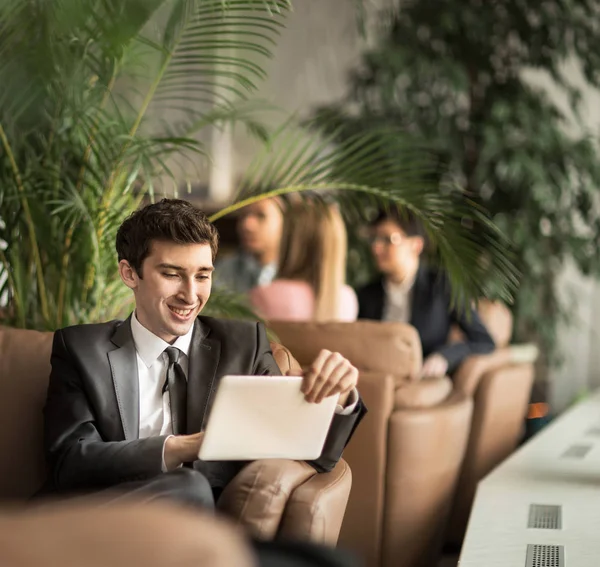 Entrepreneur-novice con una tableta digital sentada en el sofá en el vestíbulo de una oficina moderna — Foto de Stock