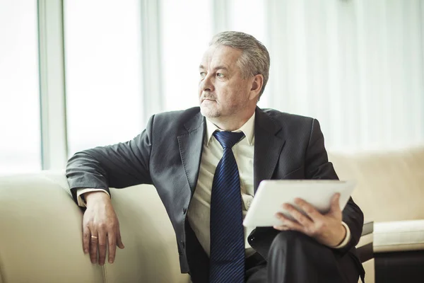 Erfaren affärsman med digital tablett sitter på soffan och tittar ut fönstret office — Stockfoto