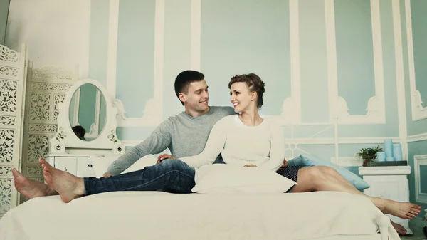 Jeune couple heureux assis au lit dans une chambre à coucher spacieuse — Photo