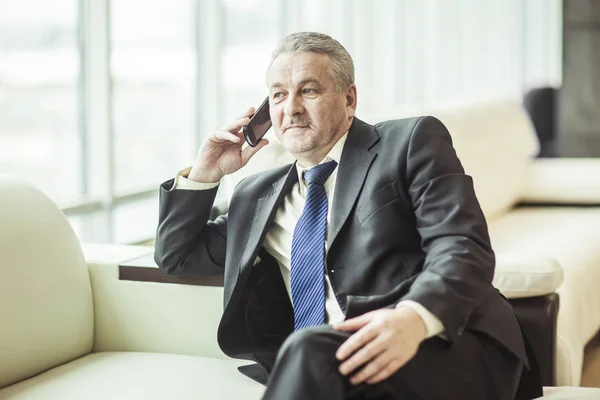 Erfolgreicher Geschäftsmann, der auf dem Sofa im Büro auf seinem Smartphone spricht — Stockfoto