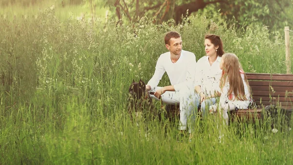 Feliz familia sentada en un banco en el parque en verano Día soleado . — Foto de Stock