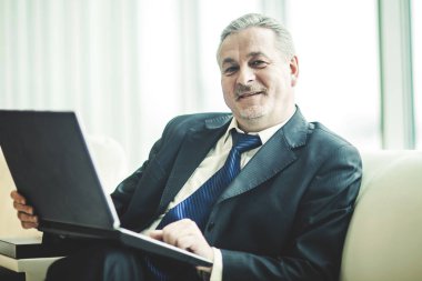 özel bir ofis kanepe üzerinde oturan dizüstü bilgisayar üzerinde çalışan deneyimli iş adamı
