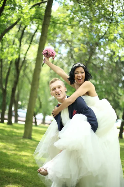 Sposo porta la sua sposa sul retro nel parco — Foto Stock