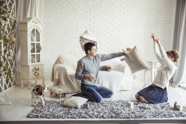 Mutlu çift şakalaşarak oturma odasındaki kanepede yastık savaşı yapıyor.