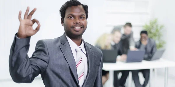 Foreground a young businessman shows gesture OK — Stock Photo, Image