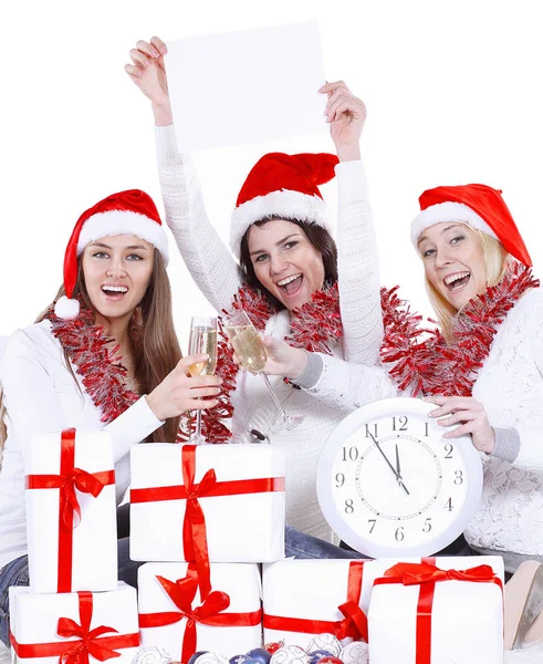 Três jovens mulheres felizes em chapéus de Papai Noel com relógio e cartaz em branco parabenizando no Natal . — Fotografia de Stock