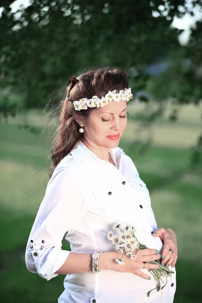 Mulher grávida feliz em uma grinalda e um buquê de flores selvagens o — Fotografia de Stock