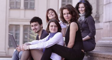 bir grup öğrenci üniversitenin önünde oturan portresi
