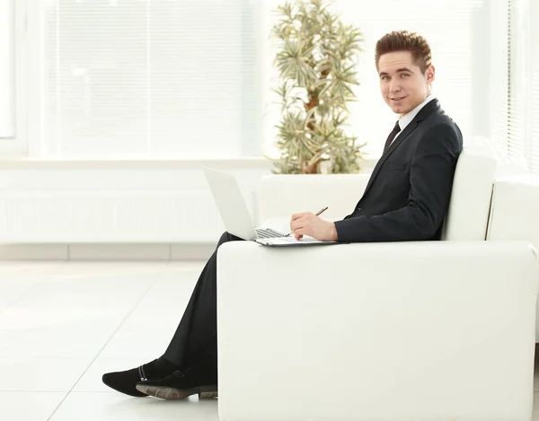 Молодий бізнесмен, що працює на ноутбуці, сидить у вестибюлі офісу — стокове фото