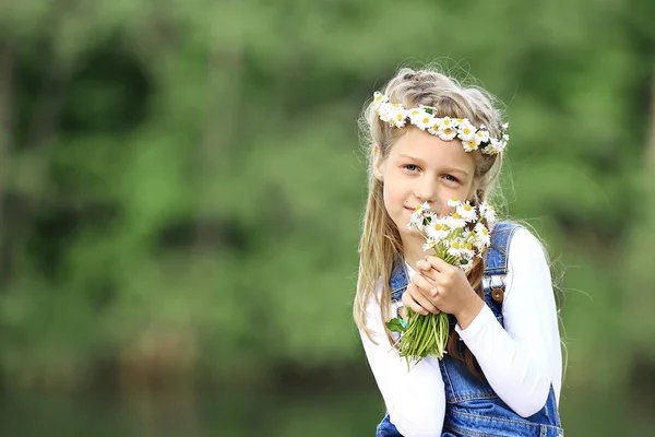 Portret van een schattig klein meisje in een krans en een boeket van wildfl — Stockfoto