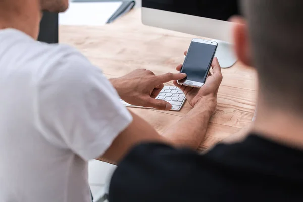 Fecha. um jovem com um smartphone sentado em sua mesa — Fotografia de Stock