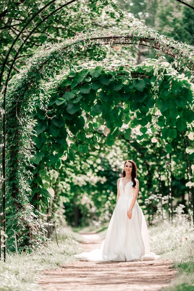 Retrato de uma noiva feliz em pé sob um arco no parque — Fotografia de Stock