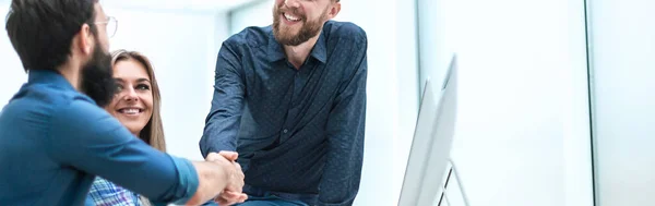 smiling co - workers shaking hands with each other at an office meeting.