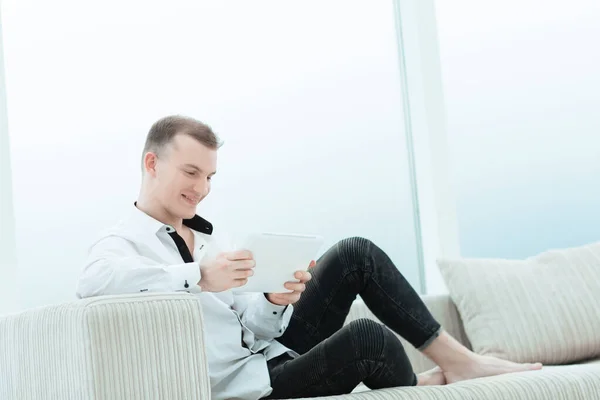 Hombre sonriente con tableta digital sentado en el sofá en su sala de estar — Foto de Stock
