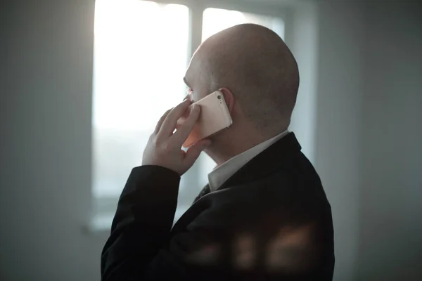 De cerca. hombre de negocios hablando en el teléfono inteligente, en el fondo borroso de la ventana de la oficina . —  Fotos de Stock