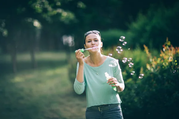 Attractive young woman playing with soap bubbles in summer Park — Stock Photo, Image