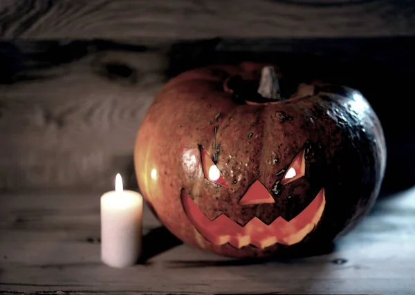 Vela y una calabaza de Halloween sonriente espeluznante en una mesa de madera —  Fotos de Stock