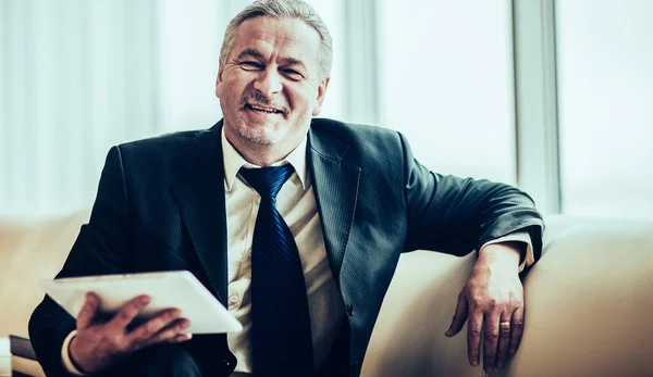 Smiling experienced businessman with digital tablet sitting on s — Stock fotografie