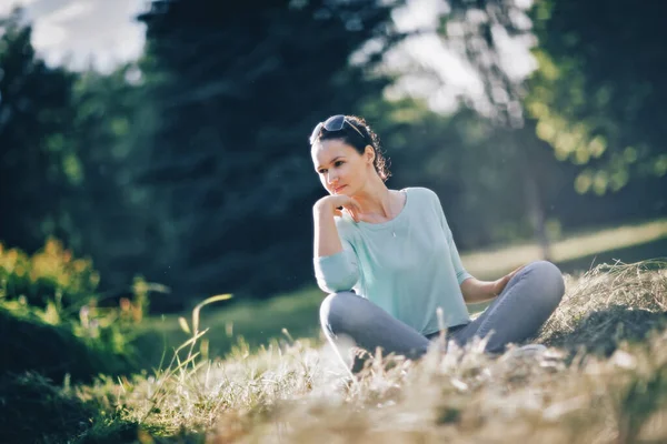 Zamyšlená mladá žena sedící v lotosové pozici v městském parku — Stock fotografie