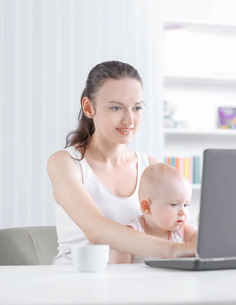 Agradável jovem mãe trabalhando sentado em casa e fazendo trabalho freelance enquanto segurando sua filha — Fotografia de Stock