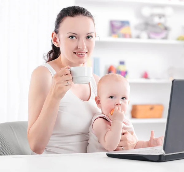 Joven mamá con pequeño bebé sentado en el Desk.the concepto de freelancing — Foto de Stock