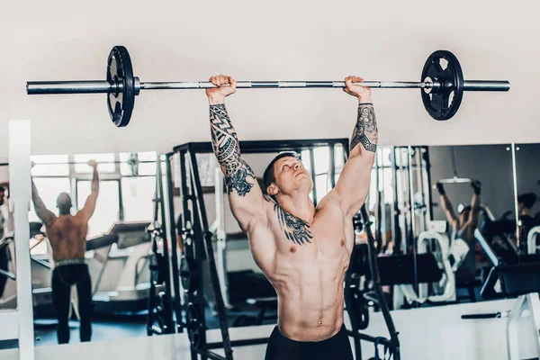 Musculoso culturista masculino hace ejercicio con una barra en el gimnasio . —  Fotos de Stock