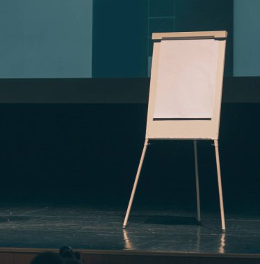 Konferans salonunun sahnesindeki beyaz ekranın önünde çevirme çizelgesi