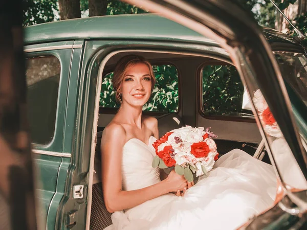 Šťastná nevěsta s kyticí sedí v autě. — Stock fotografie