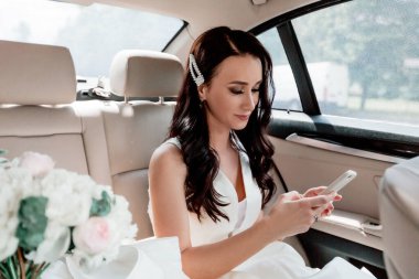Kapat. Akıllı telefonlu mutlu gelin arabada oturuyor.