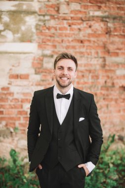 Gülümseyen damat eski tuğla duvarın arkasında.