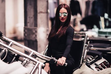 Aynalı gözlüklü, özel motosiklet üzerinde poz veren şık bir genç kadın.