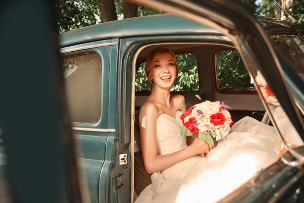 Happy bride with bouquet sitting in car. — Stock Photo, Image
