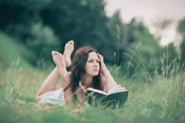 Mujer joven reflexiva con un libro acostado en el césped —  Fotos de Stock