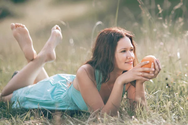 Przemyślana młoda kobieta z pomarańczą leżąca na trawniku. — Zdjęcie stockowe