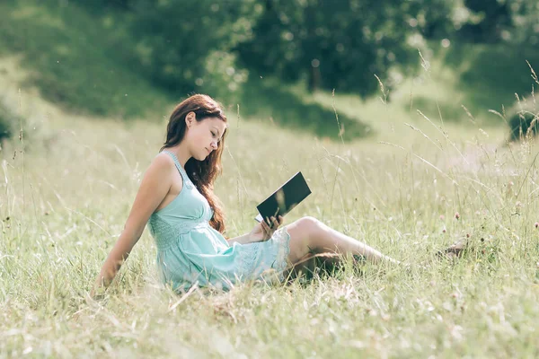 Ung kvinnlig student läser en bok som sitter på gräsmattan nära parken . — Stockfoto