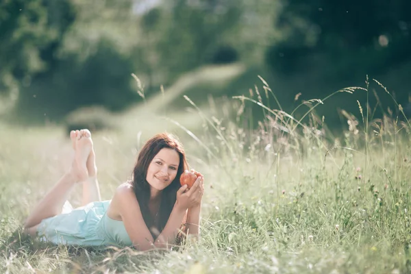 Okouzlující mladá žena s jablkem ležící na trávě a užívající si přírody — Stock fotografie