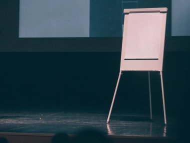 Konferans salonunun sahnesindeki beyaz ekranın önünde çevirme çizelgesi