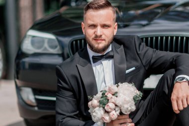 Güzel damat düğün arabasının yanında oturuyor..