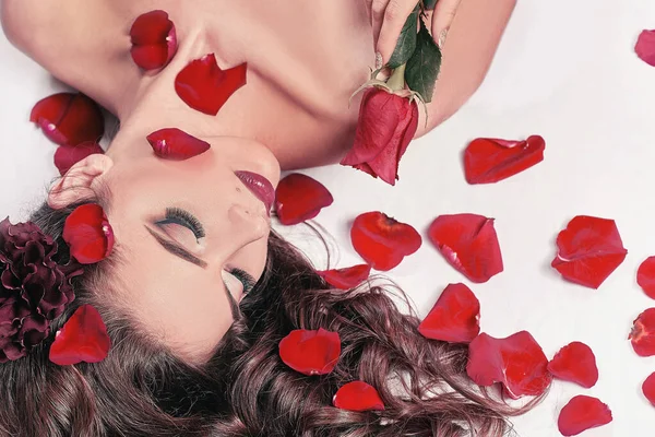 Junge Frau mit Rose zwischen Rosenblättern liegend — Stockfoto