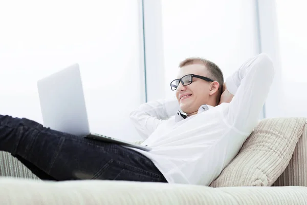 Hombre sonriente con un portátil se relaja en el sofá en su sala de estar —  Fotos de Stock
