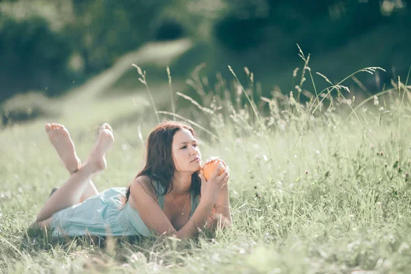 Přemýšlivá mladá žena s oranžovou relaxaci na trávníku. — Stock fotografie