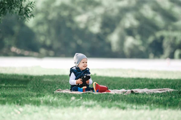Маленький мальчик играет с игрушками, сидя на лужайке в парке — стоковое фото