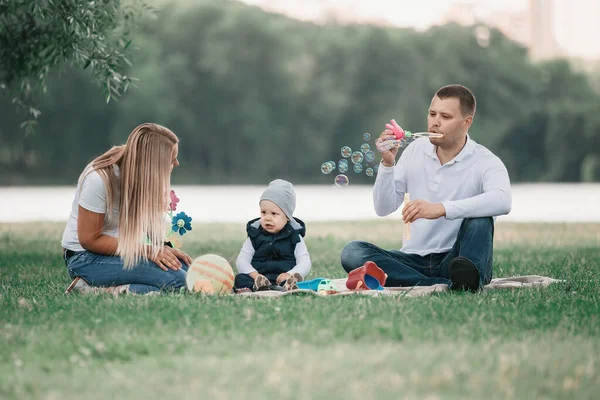 Padres y su pequeño hijo soplando burbujas en un paseo de verano . —  Fotos de Stock