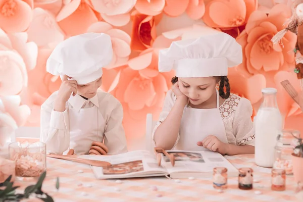 Hermano y hermana en un uniforme de chef de pie cerca de la mesa de la cocina —  Fotos de Stock