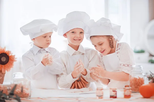 Дети в форме шеф-повара делают печенье стоя за кухонным столом — стоковое фото