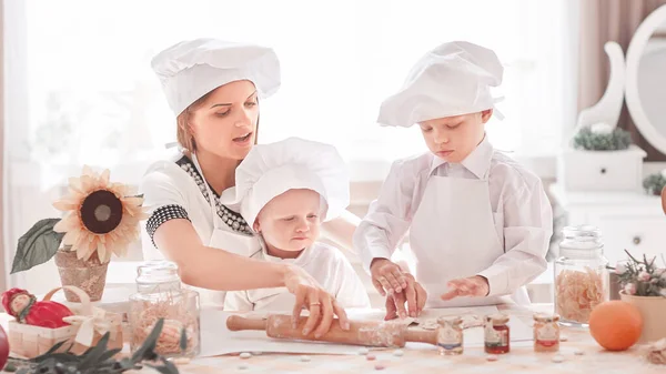 La madre feliz enseña a sus hijos a cocinar deliciosos alimentos. —  Fotos de Stock