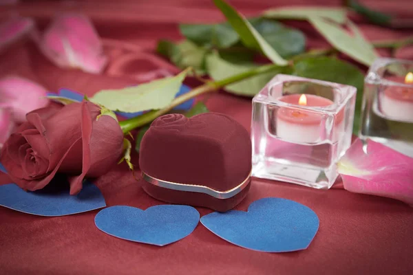 Twee kaarsen en een roos op een rode zijden achtergrond — Stockfoto