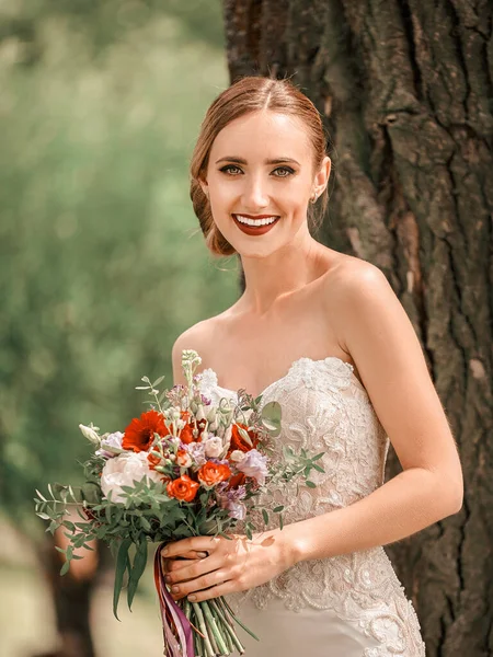 Schöne Braut steht neben einem Baum im Stadtpark — Stockfoto