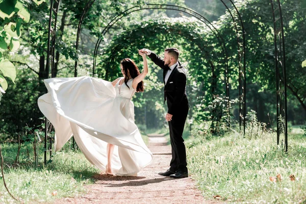 Χαρούμενη νύφη και γαμπρός χορεύουν κάτω από την γαμήλια αψίδα. — Φωτογραφία Αρχείου