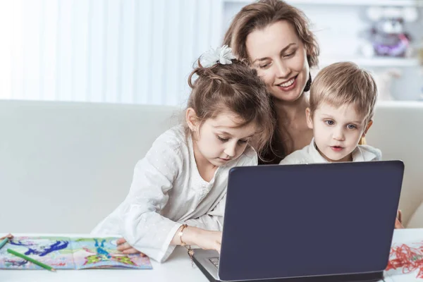 Молодая мама - деловая женщина, работающая на ноутбуке и разговаривающая на смартфоне рядом со своими детьми — стоковое фото